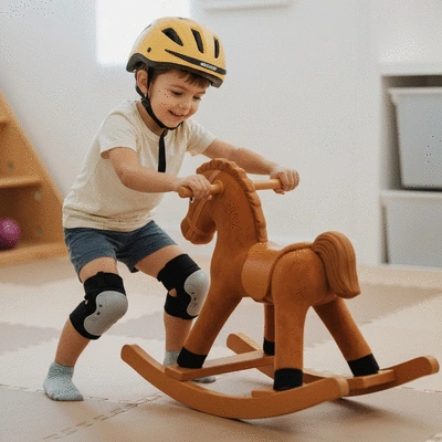 Child wearing a helmet and knee pads while playing near a rocking horse